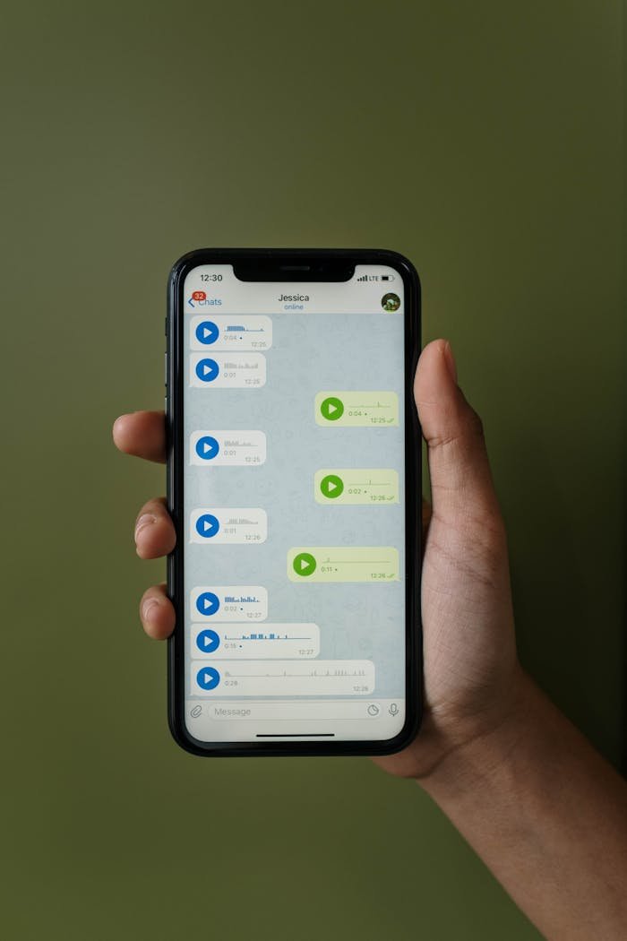 Close-up of a smartphone displaying a messaging app with voice messages in a hand.