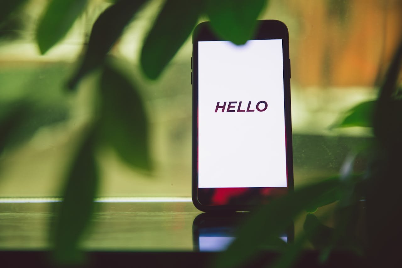 Smartphone with Hello greeting on screen surrounded by green leaves, creating a fresh and tech-savvy ambiance.
